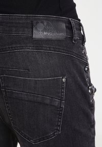 Černé denimové džíny s koženou nášivkou "MOS MOSH", bočními knoflíky a zadní kapsou s detaily prošívání.