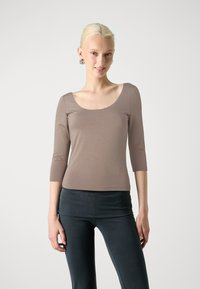 Scoop neck, fitted brown long-sleeve top paired with dark, fitted pants. The fabric appears smooth with a slight sheen.