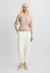 Hoodie beige à côtes avec cordon de serrage, associé à un pantalon blanc fuselé avec des accents latéraux, et des chaussures à talons dorés. Design simple et moderne.