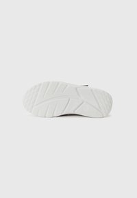 Semelle de sneaker blanche avec un grip en caoutchouc texturé, présentant un motif en zigzag et des bords arrondis. Inclus un marquage sur le côté extérieur.