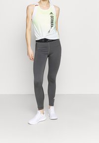 Wit en groen tanktop met de tekst "DUITSLAND", zwarte tailleband; grijze leggings met een gladde textuur; witte sportschoenen.