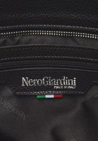 Interno in pelle nera di un prodotto NeroGiardini, con cuciture argentate, chiusura con zip e un piccolo accento con la bandiera italiana.