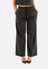 Pantaloni a palazzo neri con righe sottili, dotati di un elastico in vita e tasche laterali, realizzati in un tessuto morbido, abbinati a tacchi neri lucidi.