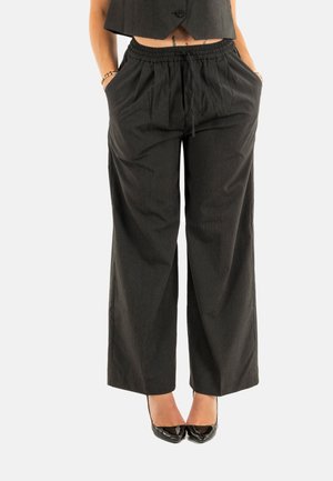 Pantalones de pata de elefante a rayas negras con cintura elástica y bolsillos laterales, confeccionados en una tela suave, combinados con elegantes tacones negros brillantes.