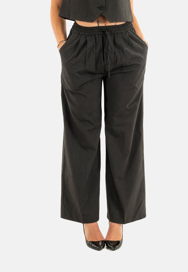 Pantaloni a palazzo neri con righe sottili, dotati di un elastico in vita e tasche laterali, realizzati in un tessuto morbido, abbinati a tacchi neri lucidi.
