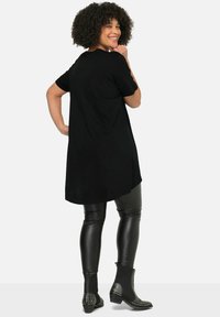 Tunique noire à manches courtes, coupe décontractée, ourlet arrière plus long, associée à des leggings noirs brillants et des bottines à clous.
