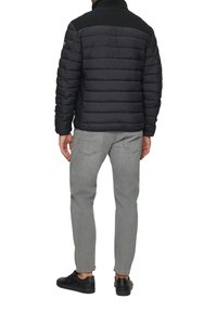 Gevoerde zwarte jas met een hoge kraag en gestructureerde zwarte schouders, gecombineerd met lichtgrijze jeans en zwarte sneakers.