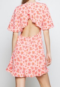 Rosa blommig klänning med korta volangärmar och öppen rygg. Har små orange och rosa blommor på ett lätt tyg. Utsvängd nederkant.