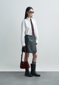 White long-sleeve shirt, dark brown tie, black leather mini skirt, gray socks, black mid-calf boots, and a burgundy handbag.