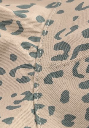 Beige szövet teal leopárdmintával. A varrat mentén látható varrás textúrát ad. Az anyag szőttnek és tartósnak tűnik.