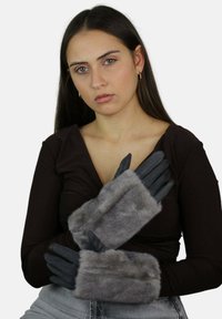 Rękawice z szarym futrzanym akcentem i czarną skórzaną podstawą, charakteryzujące się gładką strukturą oraz dopasowanym krojem, przedstawione na dłoniach skrzyżowanych na ciemnym topie.