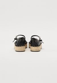 Sandales espadrilles en cuir noir avec semelles en jute tressé, sangle de cheville et détail de nœud décoratif à l'arrière. Semelle en caoutchouc pour une meilleure adhérence.