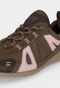 Chaussure de sport marron et rose avec lacets à motifs, empiècements synthétiques et semelle beige texturée, inclinée pour montrer les détails latéraux et avant.