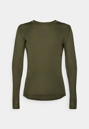 Top sportiv cu mânecă lungă, de culoare verde măslinie, fabricat dintr-un material neted și elastic. Are un gât rotund și un logo subtil pe piept.