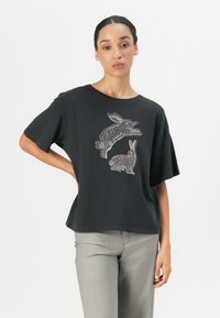 Black cotton t-shirt with short sleeves, featuring a graphic of two rabbits in light colors. Simple, relaxed shape with a round neckline.