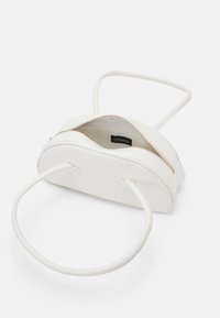 Sac à main blanc en forme de demi-lune avec des poignées fines et rondes et une fermeture éclair dorée, partiellement ouverte pour montrer la doublure intérieure en tissu et l'étiquette de la marque.