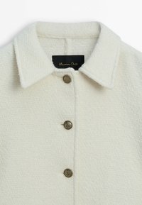 Veste en mélange de laine crème avec un col pointu, dotée de trois boutons dorés et d'une finition texturée. Étiquette visible à l'intérieur du col.