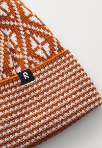 Strickmütze in Orange und Weiß, mit einem geometrischen Muster und einem einfarbigen orangen Bund. Enthält ein kleines schwarzes Etikett mit einem weißen "R."