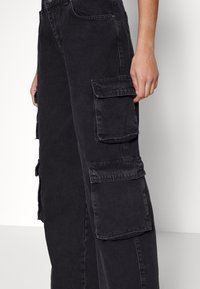 Svarta cargobyxor i denim med flera sidfickor och löst sittande passform. Tyget har en mjuk struktur med lätt blekning.