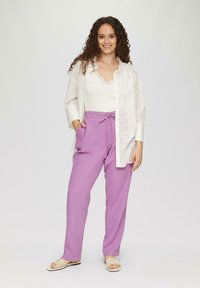 Chemise blanche avec des détails en œillets sur un débardeur clair ; associée à un pantalon lavande ample et des sandales beiges à lanières.