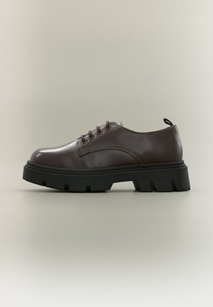 Chaussure à lacets en cuir marron foncé avec une semelle épaisse noire et robuste, œillets métalliques et languette de tirage sur fond neutre, vue de côté.