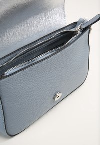 Ljusblå läderhandväska med strukturerad yta, silverdetaljer, blixtlås och kontrasterande svarta accenter längs kanterna.