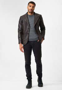 Brauner Lederblazer mit kontrastierenden Nähten, dunkelgrauer Pullover, schwarze Slim-Fit-Hose und schwarze Schnürstiefel.