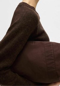 Brauner Strickpullover mit strukturiertem Finish, kombiniert mit einer dunkelbraunen, weichen Stofftasche mit glatter Oberfläche und minimalen Nähten.