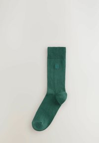Calzino in cotone verde con bordo a costine, texture liscia e tallone e punta rinforzati. Presenta un piccolo logo in rilievo vicino alla parte superiore.