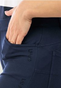 Pantaloni joggers blu navy realizzati in tessuto morbido, con una tasca laterale e logo decorato con strass. Tessuto liscio con una vestibilità comoda.
