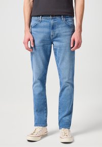 Ljust blå denimjeans med klassisk passform, med framfickor, knappgylf och subtila blekningar. Kompletteras med beiga sneakers.