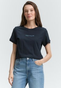 T-shirt en coton bleu marine avec des manches courtes retroussées et imprimé "TOM TAILOR EST. 1962" en bleu clair, associé à un jean taille haute bleu clair.
