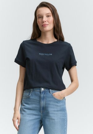 T-shirt en coton bleu marine avec des manches courtes retroussées et imprimé "TOM TAILOR EST. 1962" en bleu clair, associé à un jean taille haute bleu clair.