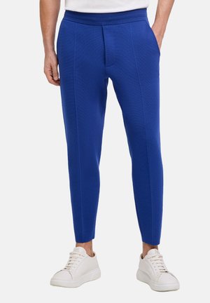 Pantaloni blu slim-fit con tessuto testurizzato, cintura elastica e tasche laterali, abbinati a sneaker bianche.