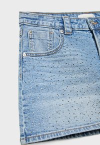 Denim krilo v svetlo modri barvi, ki se ponaša z bleščečimi kovinskimi okrasnimi elementi spredaj, ima dve žepki in kontrastne šive.