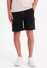 Shorts cargo noirs à coupe décontractée, avec des poches latérales et une taille à cordon de serrage, associés à des baskets blanches et un haut moucheté.
