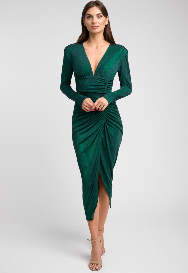 Zielona dopasowana sukienka z teksturowanej tkaniny. Długie rękawy, głęboki dekolt w serek oraz marszczenia po bokach z rozcięciem do uda. Uzupełniona o sandały na obcasie.