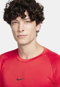 Rød atletisk skjorte med korte ærmer, lavet af glat, strækbart materiale. Har et sort Nike-logo på brystet og flade sømdetaljer.