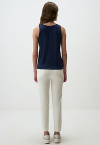Top senza maniche di colore navy abbinato a pantaloni bianchi, con un taglio dritto casual e una texture liscia. Indossato con sneakers chiare.