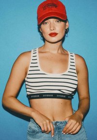 Dwukolorowy top typu crop w białe i czarne paski z kontrastującą czarną taśmą z napisem „DIVERSE”. Połączony z jasnoniebieskimi dżinsami oraz czerwoną czapką.