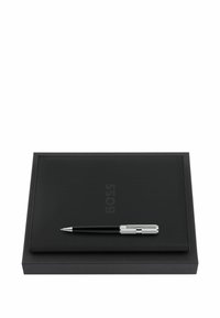 Carnet texturé noir avec logo "BOSS" en relief et stylo noir et argent reposant dessus, posé sur une boîte rectangulaire noire.