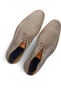 Grijze suède schoenen met bruine veters en tan leren accenten. Heeft een afgeronde neus en stiksels langs de zool. Rekbare stof bij de hak.