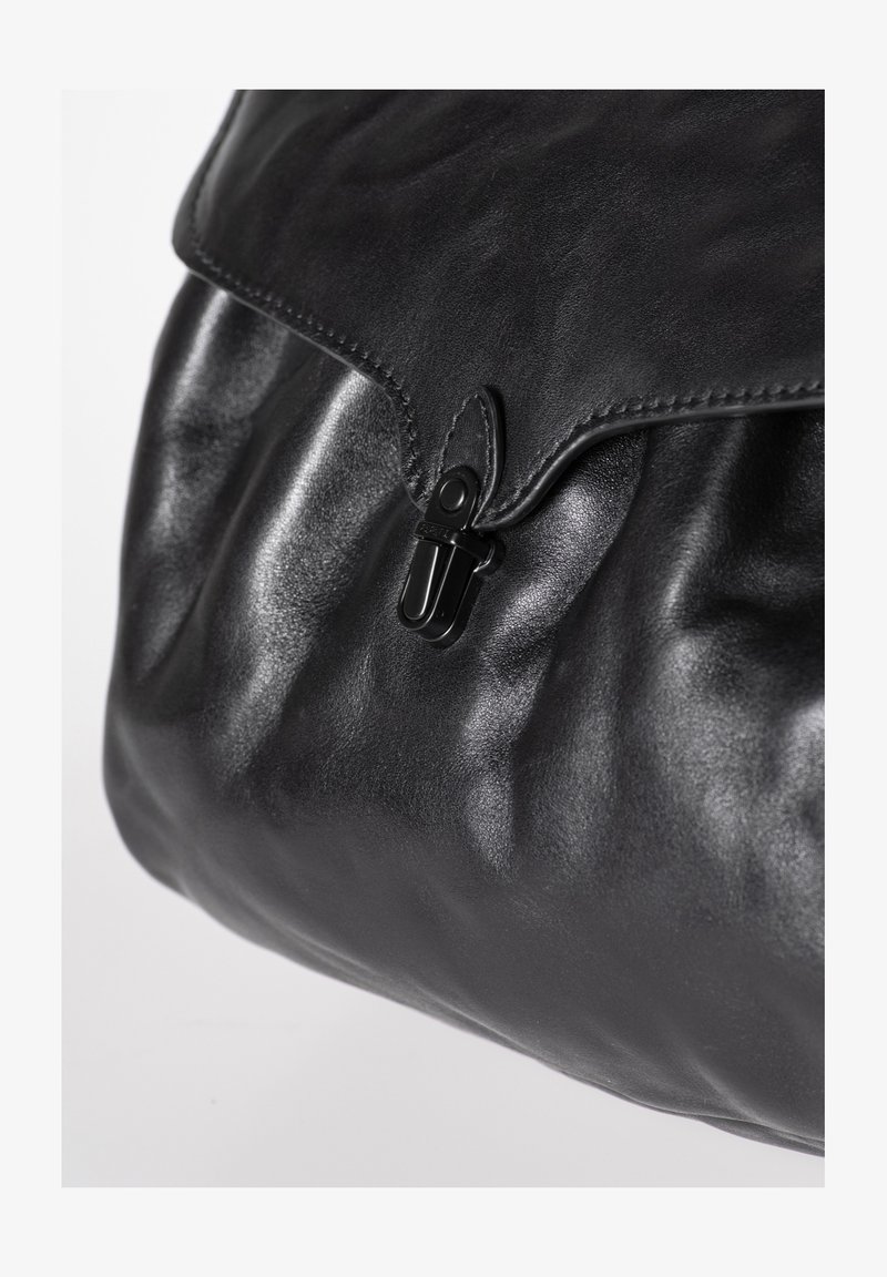 Schwarze Ledertasche mit Klappe und Verschluss aus schwarzem Metall, Nahaufnahme zeigt glatte und strukturierte Lederflächen.