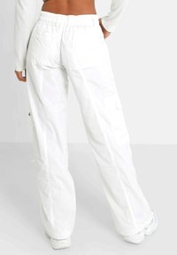 White cargo pants with a loose fit, elastic waistband, and large side pockets. Made from lightweight fabric, featuring a smooth texture.