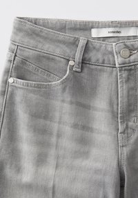 Lichtgrijze denim jeans van dichtbij met een focus op de tailleband, riemlussen, voorzak, metalen klinknagels, knop en het label "someday." aan de binnenkant van de tailleband.