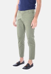 Chinos khaki in cotone con una vestibilità slim; presentano tasche frontali, chiusura con bottone e vengono indossati con scarpe slip-on scure.
