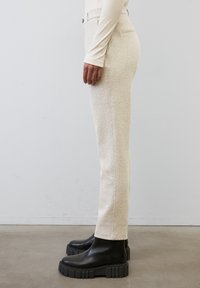 Pantalons beige à motif pied-de-poule avec une coupe slim, dotés de poches avant, d'une fermeture à bouton, associés à des bottines noires chunky.