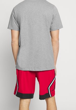 Personne portant un t-shirt gris uni à manches courtes et un short de basketball rouge avec des bordures noires et blanches, vue de dos.