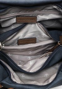 Donkerblauwe handtasinterieur met drie ritsvakken en grijze stoffen voering met een patroon van witte ronde logo's.