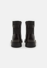Bottines noires avec un extérieur en cuir lisse et un dessus en textile. Elles présentent une fermeture éclair sur le côté et une large sangle autour de la cheville. Semelle plate.